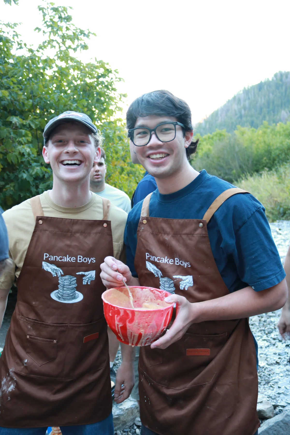 Two Pancake Boys smiling in their brown aprons with a red mixing bowl